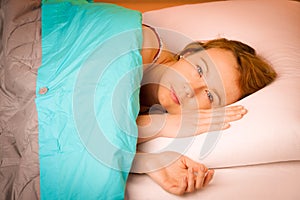Woman iling on pillow in bed, covered with blanket
