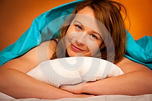 Woman iling on pillow in bed, covered with blanket