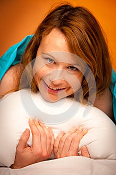 Woman iling on pillow in bed, covered with blanket