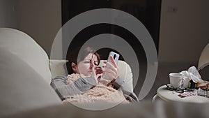 woman is ill at home, lies on the couch and uses the phone