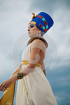 Woman in image of egyptian queen Nefertiti walks against background of sky