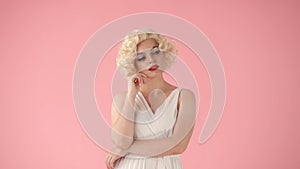 Woman in the image of Marilyn Monroe, dreamily thinking about something. Woman with bright makeup in white wig and white