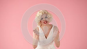 A woman in the image of Marilyn Monroe swearing in a studio against a pink background in close up. Woman pointing at you