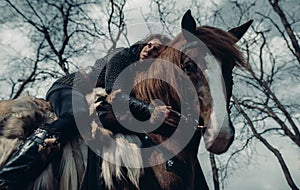 Woman in image of medieval warrior sits horseback and embraces it