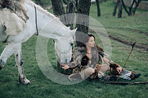 Woman in image of warrior amazon rests under tree near her horse