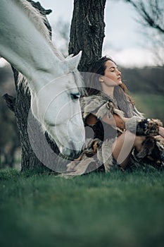 Woman in image of warrior amazon rests under tree near her horse