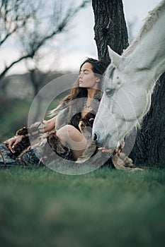 Woman in image of warrior amazon rests under tree near her horse