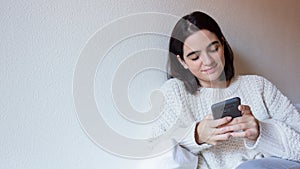 Woman indoor portrait. Young beautiful using her mobile phone. woman in warm knitted clothes at home. fashion. Autumn, winter