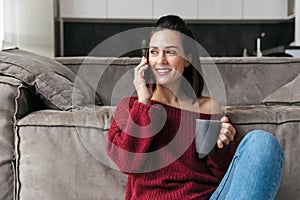Woman indoors in home talking by mobile phone drinking coffee