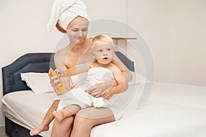 Woman and infant baby in white towels after bathing apply sunscreen or after sun lotion or cream. Children skin care in a hotel or