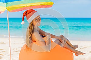 Woman on an inflatable beach couch and Christmas hat on the beach under an umbrella