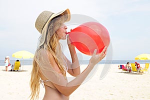 Woman inflating a red balloon on the beach