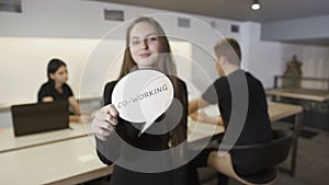 Woman with inscription `Co-working` at the background of working business team