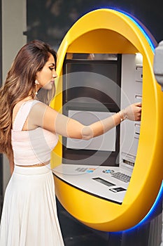 Woman insert a credit card in an ATM machine while standing outdoors on the street.