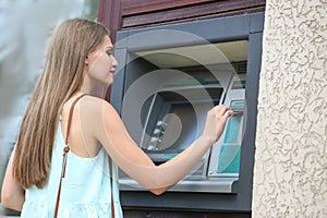 Woman inserting credit card into cash machine outdoors