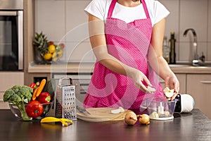 Woman inserting peeled onions into an onion chopper