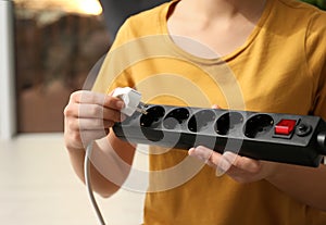 Woman inserting power plug into extension cord indoors, space for text. Electrician`s