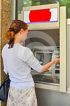 A woman inserts a plastic card into an ATM for withdrawing cash