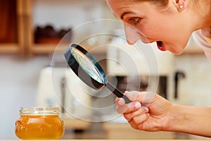 Woman inspecting honey with magnifying glass.