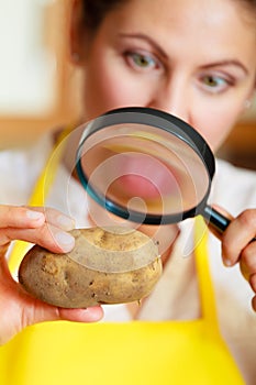 Woman inspecting potato with magnifying glass.