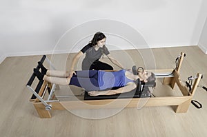 Woman and instructor in reformer bed, pilates.