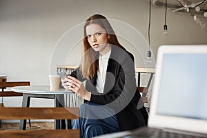 Woman is insulter with offensive words of stranger sitting with laptop. Portrait of annoyed attractive woman in cafe