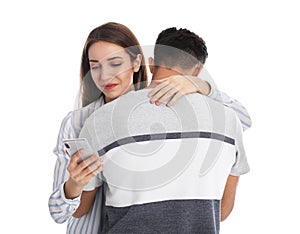 Woman interested in smartphone while hugging boyfriend on white background. Relationship problems