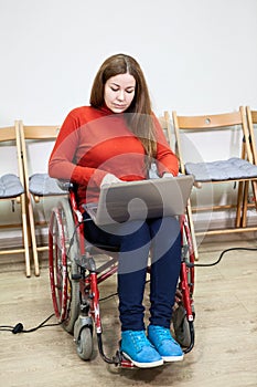 Woman in invalid wheel-chair working with laptop on knees, disabled person