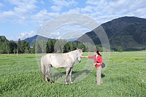 Woman ironing a horse in a meadow among the mountains