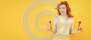 Woman isolated face portrait, banner with copy space. glad redhead girl with red heart sticks on yellow background.