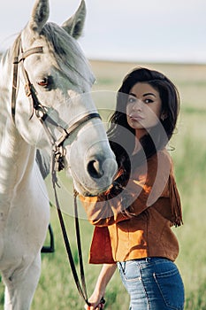 Woman in jacket holds horse by the bridle on meadow