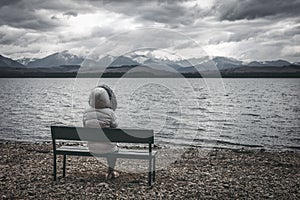 Woman in jacket sitting on bench on the shore of the lake