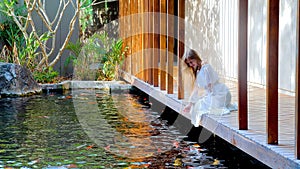 Woman on wooden bridge in Japanese garden feeding fish