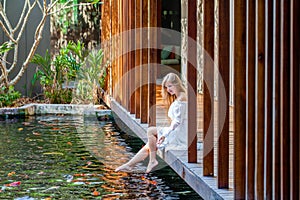 Woman on wooden bridge in Japanese garden feeding fish