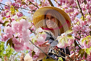 woman with a Japanese hat next to a blooming cherry tree