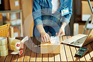 Woman in jeans applying shipping label to parcel in warehouse