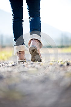 Woman in jeans and boots walking along a rural path