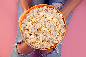 Woman in jeans holding bowl with popcorn over pink background