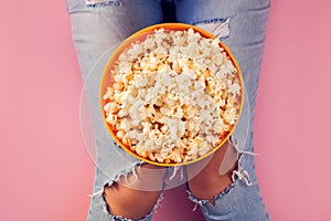 Woman in jeans holding bowl with popcorn over pink background