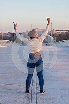 a woman in jeans is raising her arms and a city in the background