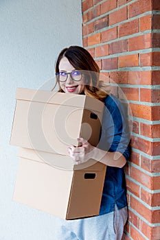 Woman in jeans shirt standing on brick wall with moving boxes
