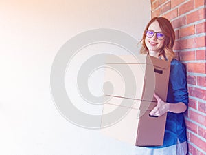Woman in jeans shirt standing on brick wall with moving boxes