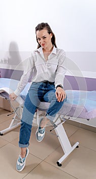 Woman in jeans sitting on couch. Nurse in scrubs on the background. Happy and smiling girl at doctor s.