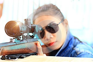 Woman in jeans suit and wearing sunglasses with the shooting range shot from a rifle gun