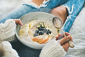 Woman in jeans and sweater eating healthy oatmeal porriage