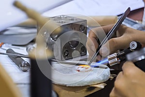 Woman jeweller, designer holding blowtorch and making handmade brooch - close up