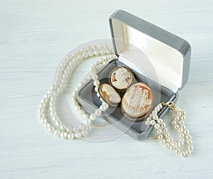 Woman Jewelry. Vintage jewelry background. Beautiful pearl necklace, bracelet and old cameos in a gift box on white wood. Flat