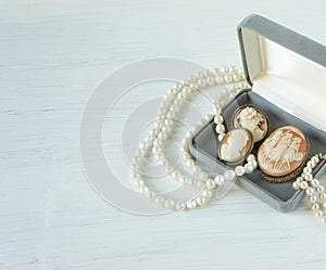 Woman Jewelry. Vintage jewelry background. Beautiful pearl necklace, bracelet and old cameos in a gift box on white wood. Flat