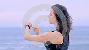 Woman jogger on beach doing exercises and looking data on fitness watch
