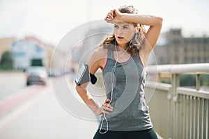 Woman jogger taking a break on bridge while wiping forehead